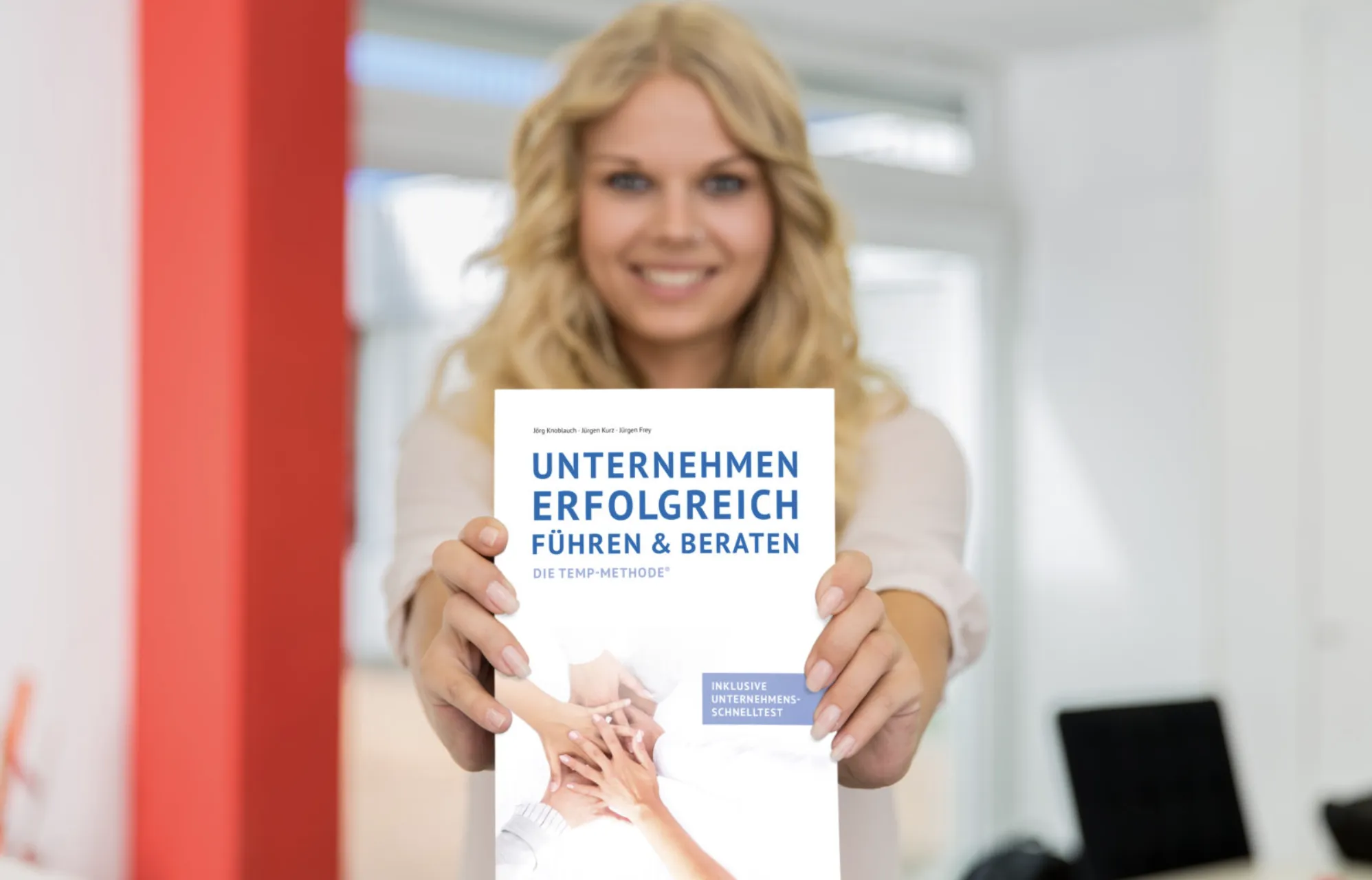 Lächelnde Frau hält das Buch „Unternehmen erfolgreich führen & beraten“ direkt in die Kamera.